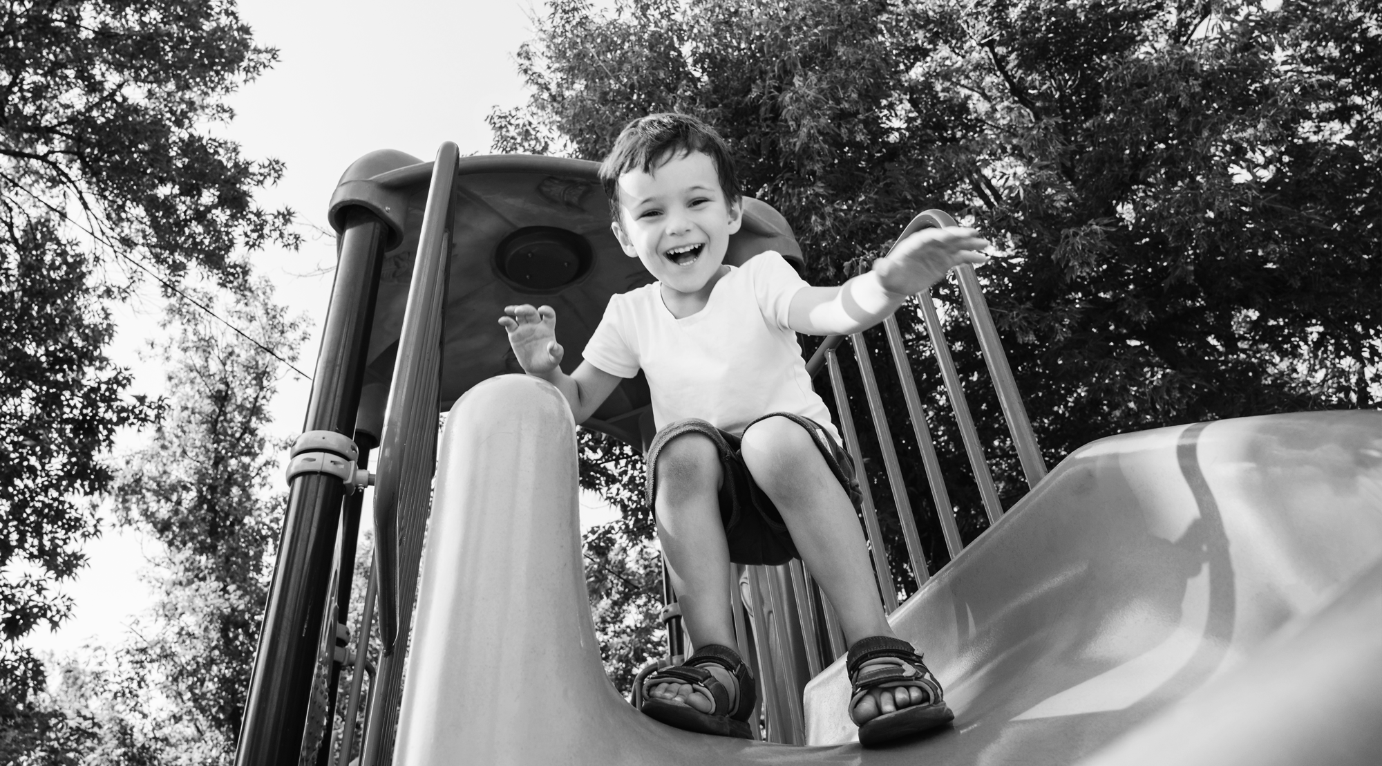 Young boy, happy at playground, coming down a slide.